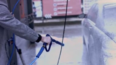 Otomobil yıkamada yüksek basınçlı su teçhizatıyla araba temizleme işlemi. Vitiligo giysili genç adam arabasını foarm ile temizliyor. 4K video