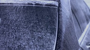 Tanınmayan kişi yüksek basınçlı jet suyu ile oto yıkamada arabadaki köpüğü ve tozu yıkar. Arabanın yüzeyinden köpüklü deterjan çekilir. 4K video