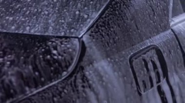 Tanınmayan kişi yüksek basınçlı jet suyu ile oto yıkamada arabadaki köpüğü ve tozu yıkar. Arabanın yüzeyinden köpüklü deterjan çekilir. 4K video