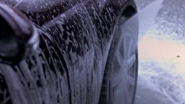 Tanınmayan kişi yüksek basınçlı jet suyu ile oto yıkamada arabadaki köpüğü ve tozu yıkar. Arabanın yüzeyinden köpüklü deterjan çekilir. 4K video