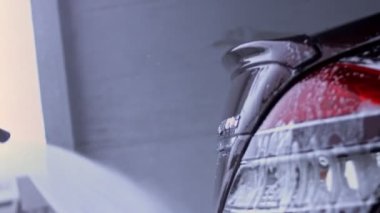 Tanınmayan kişi yüksek basınçlı jet suyu ile oto yıkamada arabadaki köpüğü ve tozu yıkar. Arabanın yüzeyinden köpüklü deterjan çekilir. 4K video