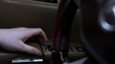 Kolluktaki el, arabanın kapısındaki elektrikli yükseltme mekanizmasının düğmelerine basar. Lüks araba iç mekanı. - Yakın çekim. 4K video