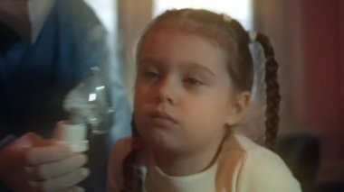 Güzel küçük kız hastanede kompresör spreyi kullanarak solunum yapıyor. Beş yıl oldu. Yüzünde nebulizör maskesiyle salin buharı soluyan bir kız. Doktor küçük kızın hastanede nefes almasına yardım ediyor.