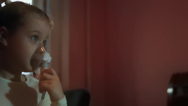 Kleines Mädchen inhaliert mit einem Kompressor, während es auf einem Sofa sitzt. 5 Jahre Sie selbst trägt eine Vernebelungsmaske und inhaliert Salzdämpfe. 4K-Video — Stockvideo