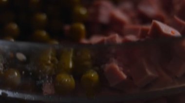 Geleneksel Rus salatası Olivier 'i hazırlıyorum. Cam bir kasenin içindekiler - yeşil bezelye, patates, sosis, havuç, yumurta. 4K video