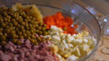 Geleneksel Rus salatası Olivier 'i hazırlıyorum. Cam bir kasenin içindekiler - yeşil bezelye, patates, sosis, havuç, yumurta. 4K video