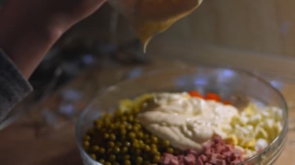 Het bereiden van Russische traditionele salade Olivier. Het toevoegen van mayonaisse aan andere ingrediënten in een glazen kom - groene erwten, aardappelen, worst, wortel, eieren. 4K-video — Stockvideo