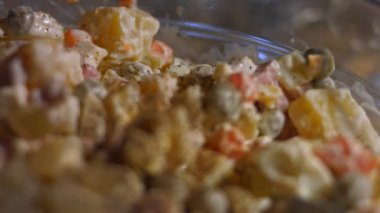 Geleneksel Rus salatası Olivier 'i hazırlıyorum. Yeşil bezelye, salatalık, patates, sosis, havuç, yumurta, mayonez. Tuz ve biberle tatlandırılmış. 4K video