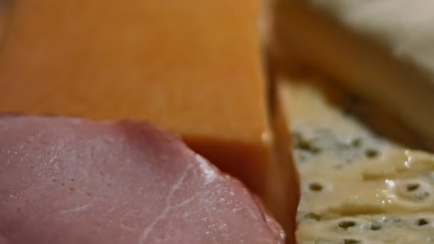Forskjellige typer smakfulle og ferske oster og svinekjøtt-skinke klare til å klippes som forrett, 4K-video – stockvideo