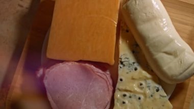 Çeşitli baharatlı ve taze peynirler ve meze olarak dilimlenmeye hazır domuz jambonu, 4K video. Yavaş çekim, üst görünüm