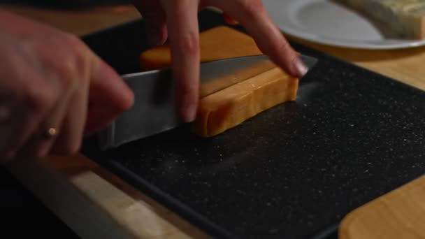 Bloque de queso cheddar que se corta en una tabla de cortar. Queso cheddar en cubitos como sabroso aperitivo. Vídeo 4K — Vídeos de Stock