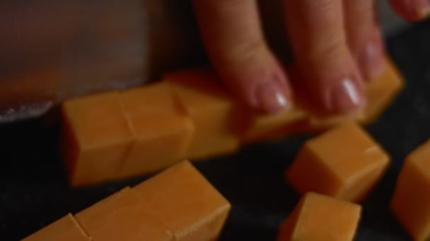 Bloco de queijo Cheddar sendo cortado em uma tábua de corte. Queijo cheddar em cubos como aperitivo saboroso. Vídeo 4K — Vídeo de Stock