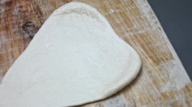 Tahta kesme tahtasının üzerinde pizza için taze hamur hazırlıyorum. Sevgililer Günü için kalp şeklinde pizza hazırlıyorum. Sevdiğim biri için. 4K video. Sanatsal çekim