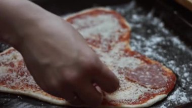 Fırın tepsisindeki kalp şeklindeki hamurun içindeki diğer malzemelere Milano salam sosisi ekliyorum. Sevgililer Günü için kalp şeklinde pizza hazırlıyorum. Sevdiğim biri için. 4K video. Sanatsal çekim