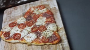 Tahtada sıcak kalp şeklinde pizza. Sevgililer Günü 'nde sevdiklerine sürpriz yemek. 4K video. Üst görünüm, döndürme
