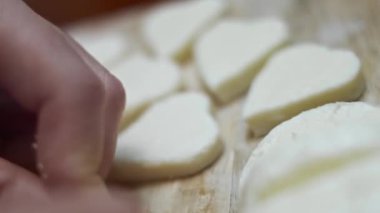 Ahşap kesme tahtasının üzerinde kalp şeklinde mozzarella peyniri kesen kadın elleri. Sevgililer Günü için yemek hazırlıyorum. 4K video. Sanatsal çekim