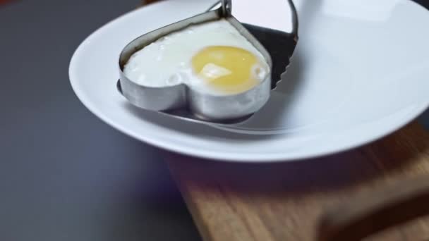 Stekt kyckling ägg, form i form av ett hjärta, sätta på en tallrik. Mat till alla hjärtans dag. Begreppet rolig överraskning för en nära och kära för ett speciellt tillfälle. 4K-video — Stockvideo