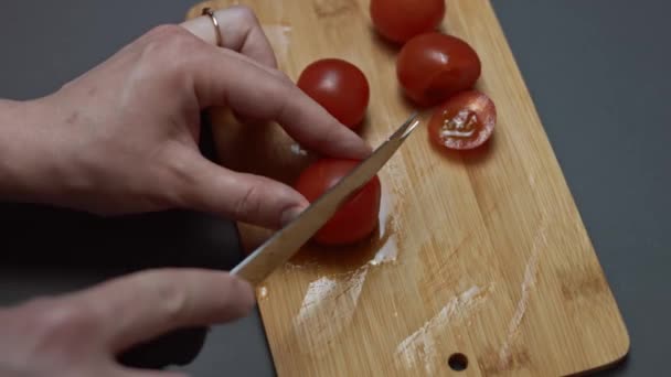 Le mani femminili tagliano pomodori ciliegia su dimezzato con un coltello su un tagliere di legno. Video 4K — Video Stock