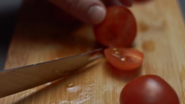 Las manos femeninas cortan los tomates cherry por la mitad con un cuchillo en una tabla de cortar de madera. Unir dos mitades de tomates cherry con un pincho de madera. Vídeo 4K — Vídeos de Stock