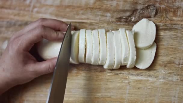 Manos femeninas rebanando queso mozzarella en una tabla de cortar de madera. Vídeo 4k. Vista superior — Vídeos de Stock