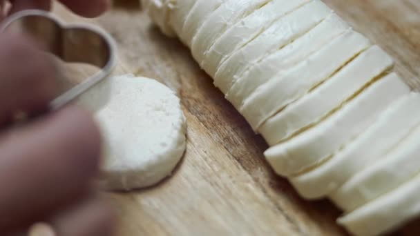 Las manos femeninas cortan las formas del corazón del queso mozzarella en una tabla de cortar de madera. Preparando comida para el Día de San Valentín. Vídeo 4k — Vídeos de Stock
