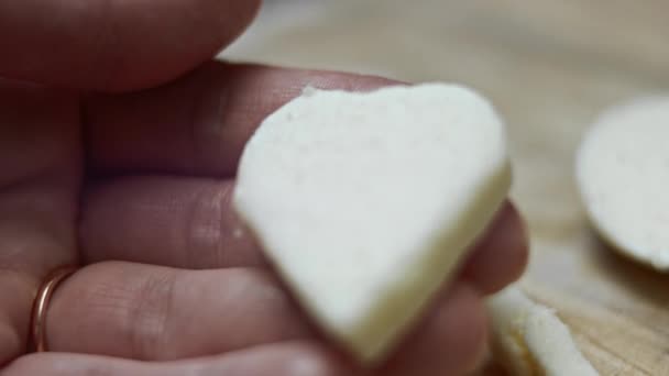 Mano femenina sosteniendo una forma de corazón de queso mozzarella sobre un fondo de tabla de cortar de madera. Preparando comida para el Día de San Valentín. Vídeo 4k — Vídeos de Stock