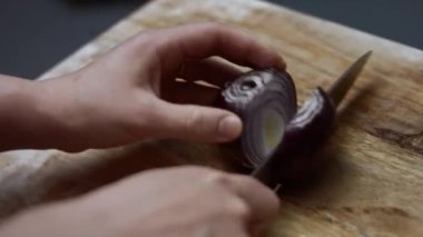 Dişi eller, tahta kesme tahtasıyla taze kırmızı soğanı ikiye bölüyor. 4K video. Sanatçı çekimi