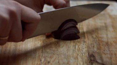 Ahşap bir kesme tahtasının üzerinde taze kırmızı soğanın yarısını dilimleyen kadın elleri. 4K video. Sanatçı çekimi