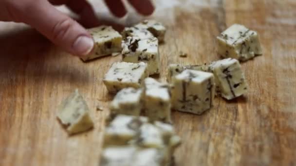 Queijo azul dinamarquês. Close-up de mão feminina separando cubos de queijo mycella em uma placa de corte de madeira. Vídeo 4K — Vídeo de Stock