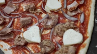 Makro kalp manzarası içerikli pizza hamuru şeklinde. Sevgililer Günü için kalp şeklinde ton balıklı pizza hazırlıyorum. 4K video. Üst görünüm, döndürme