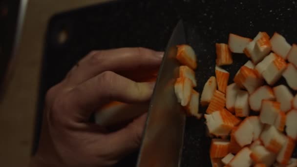 Vertikale Ansicht einer Frau, die Krabbenstäbchen für Salat auf einem Schneidebrett schneidet. Zubereitung von Salat aus Krabbenstangen, Käse, Gurken, Maiskonserven und Eiern in der heimischen Küche — Stockvideo