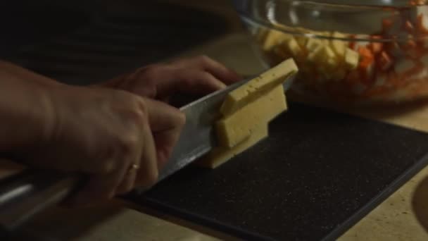 Kesme tahtasına peynir dilimlemek. Evde mutfakta yengeç çubuğu, peynir, salatalık, konserve mısır ve yumurta salatası hazırlıyorum. — Stok video