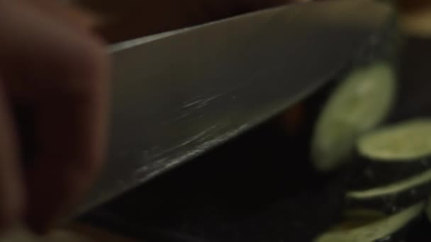 Corte de pepinos frescos em tábua de corte de madeira com faca. Preparando salada de palitos de caranguejo, queijo, pepino, milho enlatado e ovos na cozinha em casa. Tiro artístico — Vídeo de Stock
