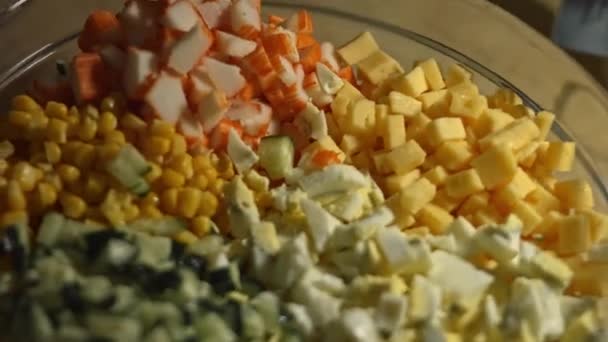 Crab salad ingredients in a glass bowl. Preparing salad of crab sticks, cheese, cucumber, canned corn and eggs in the kitchen at home. Artistic shooting — Stock Video