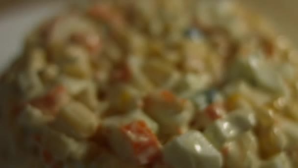 Krabí salát na talíři zdobeném strouhaným sýrem. Salát z krabích tyčinek, sýrů, okurek, konzervované kukuřice, majonézy a vajec doma v kuchyni. Umělecká střelba — Stock video