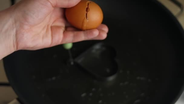 Matlagning stekt ägg i form av hjärta. Att knäcka ett ägg ovanför en stekpanna. Matlagning en överraskning frukost för Mars, 8. Konstnärlig fotografering — Stockvideo