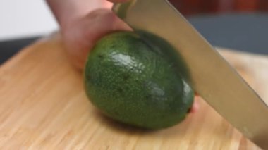 Ahşap bir kesme tahtasıyla bir kadın avokadoyu ikiye bölüyor. 8 Mart 'ta sürpriz kahvaltı hazırlıyorum. Sanatsal çekim