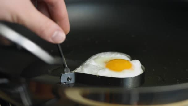 Cuire des œufs frits en forme de cœur dans une poêle. Mettre l'œuf dans une assiette. Cuisiner un petit déjeuner surprise pour Mars, 8 — Video