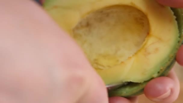 Weibliche Hände entfernen mit einem Löffel die Schale einer Avocado. Kochen eines Überraschungsfrühstücks für den 8. März — Stockvideo