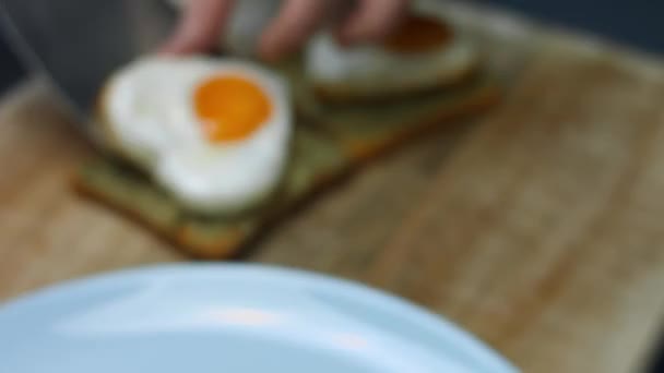 Colocar ovos em forma de coração em torradas com abacate esmagado numa tábua de madeira. Cozinhar um café da manhã surpresa para março, 8 — Vídeo de Stock