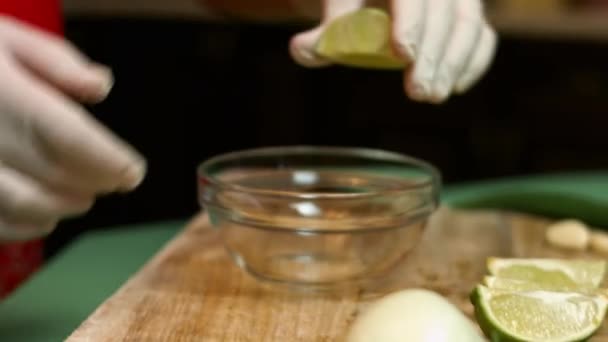 Kvinnliga händer klämmer åt en färsk lime. Droppar limejuice faller ner i en glasskål. Processen att göra salsa. Konstnärlig fotografering — Stockvideo