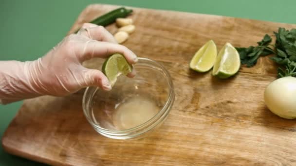 Las manos femeninas exprimen la lima fresca. Gotas de jugo de lima caen en un tazón de vidrio. Proceso de hacer salsa — Vídeo de stock