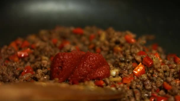 Lägga till tomatpuré och vatten till marken nötkött och röd paprika matlagning på en stekpanna. Blandning med en träspatel. Process för att göra quesadillas — Stockvideo