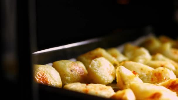 Las manos femeninas ponen la bandeja para hornear con papas doradas asadas especiadas con aceite, sal y pimienta negra de vuelta en el horno. Proceso de cocción de patatas asadas al horno perfecto — Vídeos de Stock