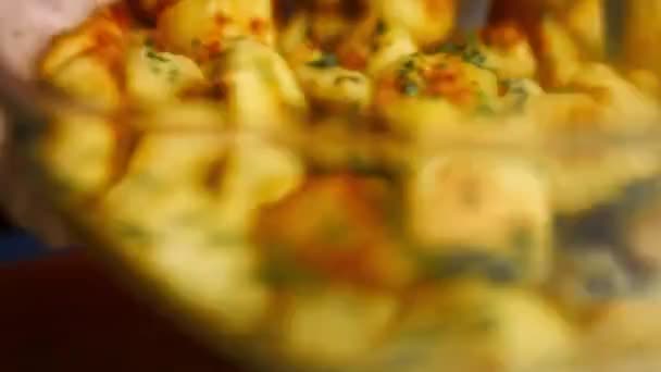 Agitare la ciotola di vetro per mescolare le patate dorate arrosto speziate con aglio fritto e rosmarino e prezzemolo fresco. Processo di cottura patate arrosto perfetto forno. Vista macro — Video Stock