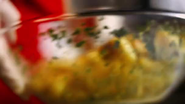Agitare la ciotola di vetro per mescolare le patate dorate arrosto speziate con aglio fritto e rosmarino e prezzemolo fresco. Processo di cottura patate arrosto perfetto forno — Video Stock