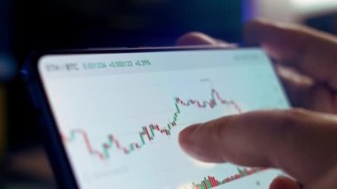 Çay içerken akıllı telefondan şifreli para grafiği analiz ediliyor. Borsada BTC 'den alıntılar. Akıllı telefondaki uygulamayı ekranda görüntüle. Makro görünüm