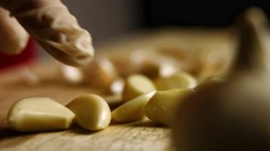 Eldiven giymiş kadın eller soyulmuş karanfilleri sayıyor ve tahta kesme tahtasından biraz daha soyuluyor. Pişirme işlemi shkmeruli - Gürcü yemeği. Makro görünüm