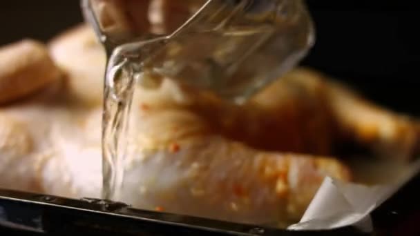 Femme chef versant un verre d'eau sur une plaque à pâtisserie avec un gros poulet cru salé assaisonné, se préparant à être cuit. Processus de cuisson shkmeruli - plat géorgien — Video