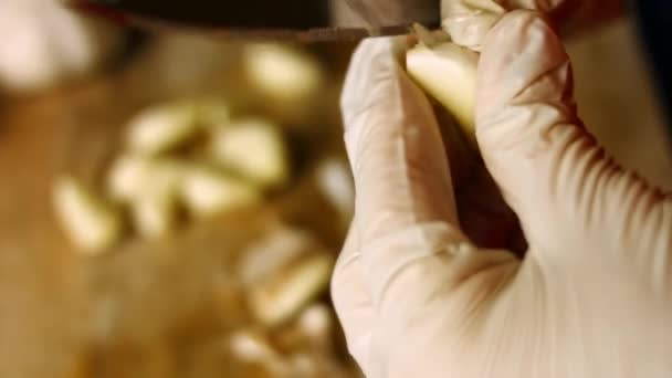 Женские руки в перчатках чистят чеснок гвоздикой над деревянной разделочной доской. Процесс приготовления шкмерули - грузинское блюдо. Макровзгляд — стоковое видео